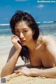 A naked woman laying on a sandy beach.