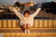 A woman sitting on top of a building with her arms outstretched.